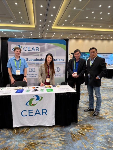 Group of four people standing behind a CEAR table at an event with a branded backdrop.