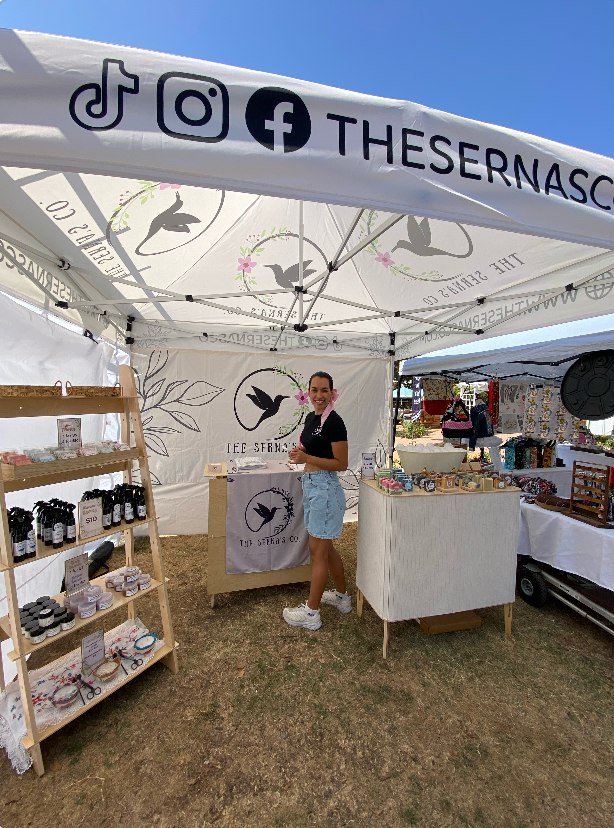Person standing under a branded tent with shelves and tables displaying products.